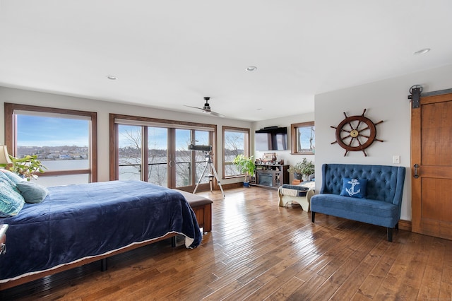 bedroom featuring wood-type flooring, a barn door, a water view, and ceiling fan