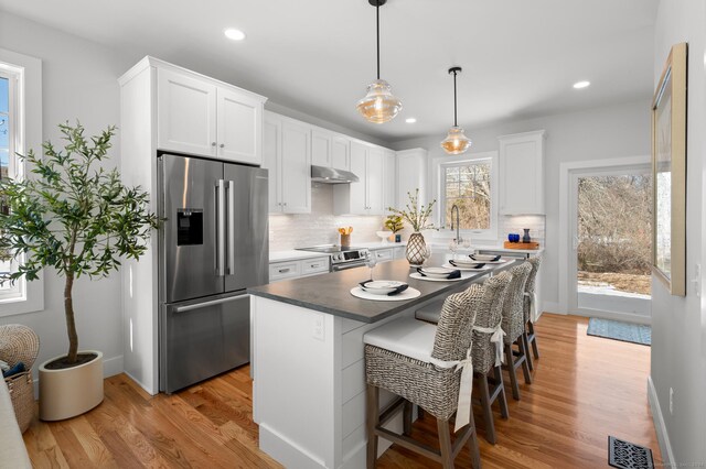 kitchen featuring stainless steel appliances, white cabinets, light hardwood / wood-style floors, a kitchen island, and a breakfast bar area