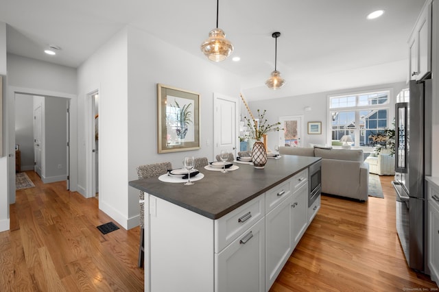 kitchen featuring appliances with stainless steel finishes, light wood-type flooring, white cabinets, a center island, and hanging light fixtures