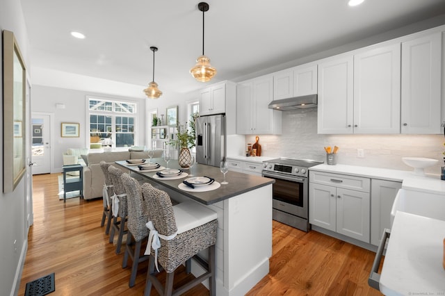 kitchen with white cabinetry, stainless steel appliances, decorative light fixtures, a kitchen bar, and light wood-type flooring