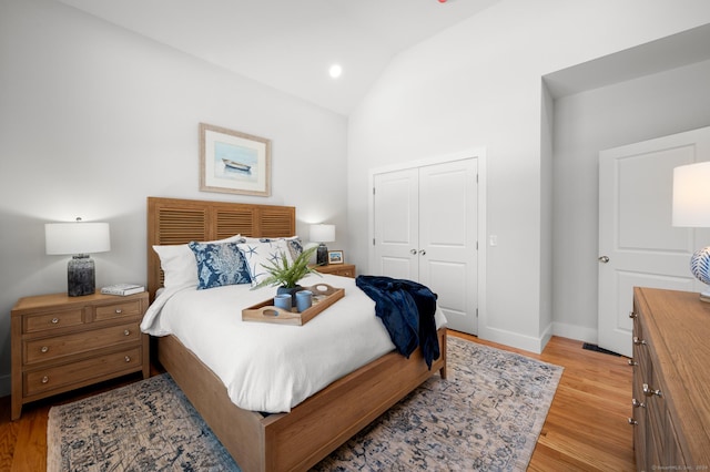 bedroom with light wood-type flooring, vaulted ceiling, and a closet