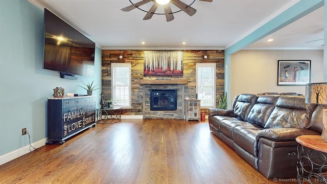 living room with a stone fireplace, crown molding, hardwood / wood-style floors, and ceiling fan