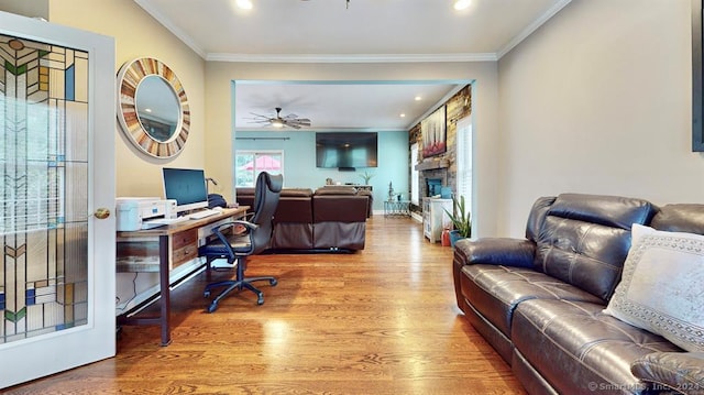 office area with wood-type flooring, a stone fireplace, ceiling fan, and ornamental molding