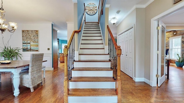 stairs featuring hardwood / wood-style flooring, crown molding, and a notable chandelier