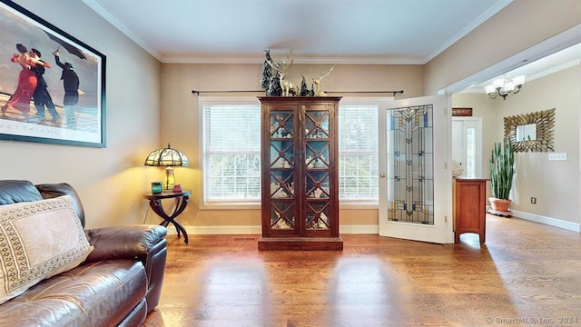 sitting room with wood-type flooring, an inviting chandelier, and crown molding