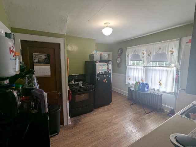 kitchen with dark wood-type flooring, black appliances, and radiator heating unit