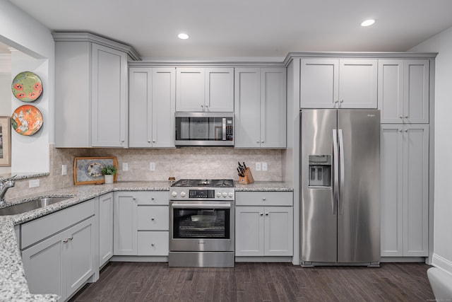 kitchen with sink, dark wood-type flooring, stainless steel appliances, tasteful backsplash, and light stone counters