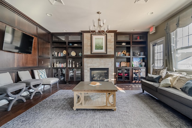 living room featuring a chandelier, built in shelves, a fireplace, and dark wood-type flooring