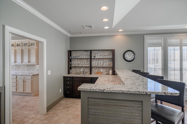 kitchen with light stone countertops, ornamental molding, tasteful backsplash, cream cabinetry, and a breakfast bar area