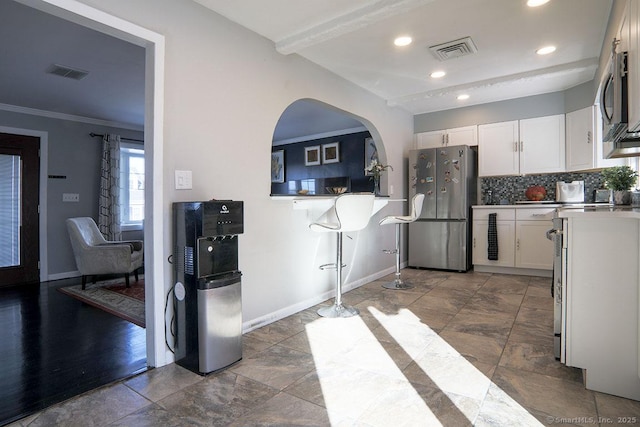 kitchen featuring decorative backsplash, white cabinetry, appliances with stainless steel finishes, and crown molding