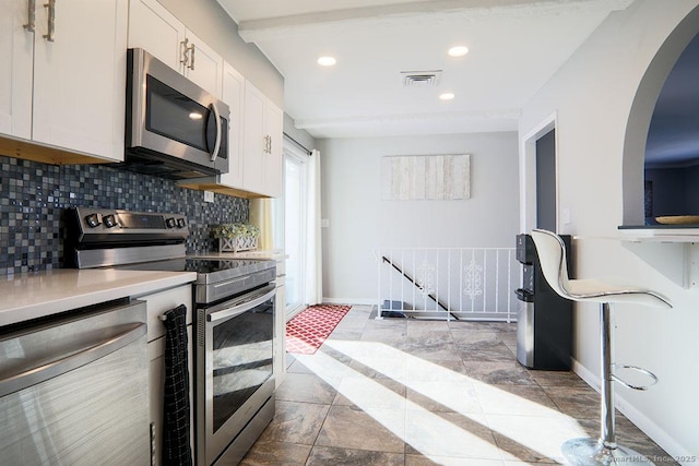 kitchen featuring light tile patterned flooring, appliances with stainless steel finishes, white cabinets, and tasteful backsplash