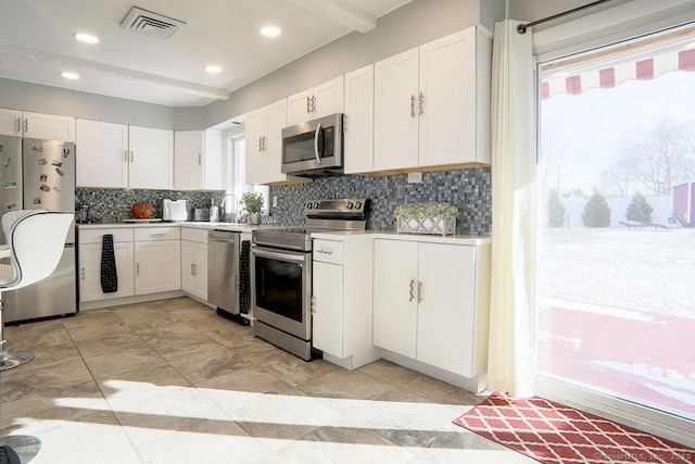 kitchen with white cabinets, decorative backsplash, appliances with stainless steel finishes, and beamed ceiling