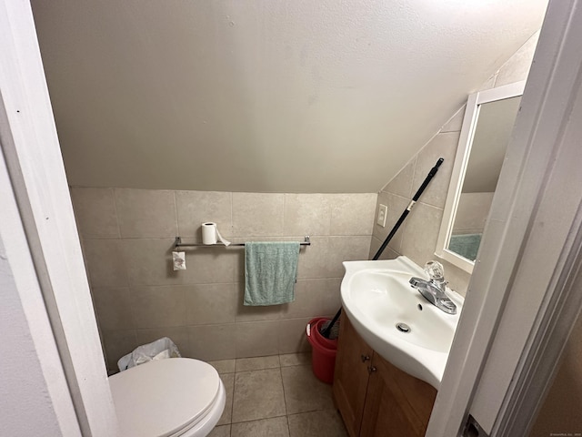 bathroom with tile patterned floors, vanity, vaulted ceiling, tile walls, and toilet