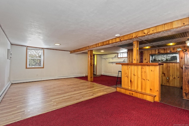 basement featuring bar, hardwood / wood-style flooring, wood walls, and a baseboard heating unit