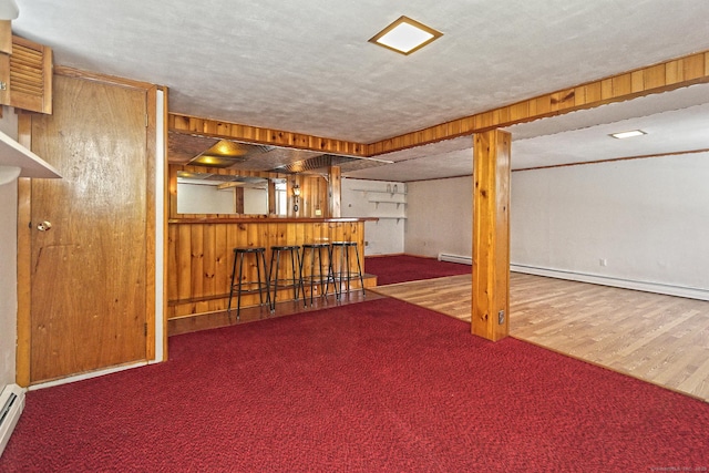 basement featuring a textured ceiling, indoor bar, a baseboard heating unit, and wood walls