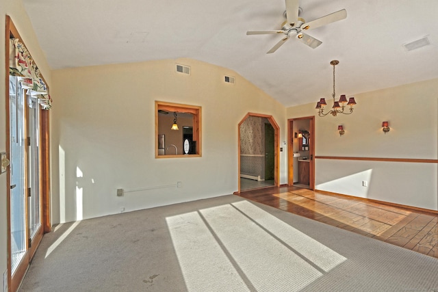 carpeted spare room featuring ceiling fan with notable chandelier and vaulted ceiling