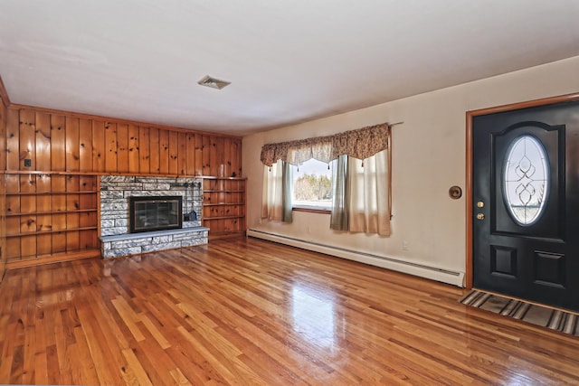 unfurnished living room with a fireplace, a baseboard radiator, light hardwood / wood-style flooring, and wood walls