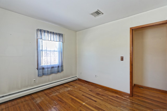 empty room with dark hardwood / wood-style flooring and a baseboard heating unit