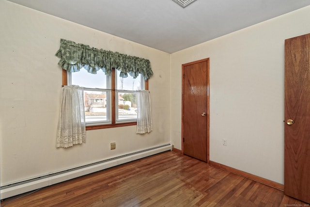 empty room featuring baseboard heating and hardwood / wood-style flooring