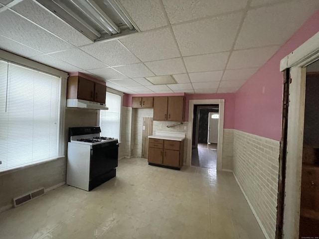 kitchen featuring a drop ceiling, white gas range, and brick wall