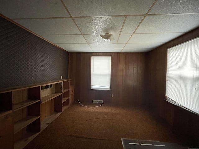 empty room featuring carpet flooring, a paneled ceiling, and wood walls