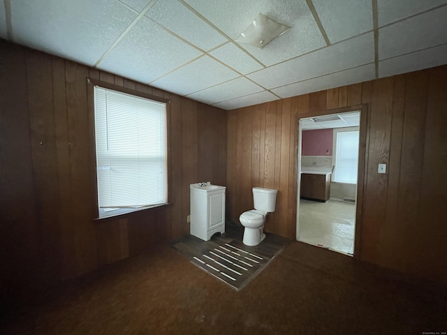 bathroom with toilet, a drop ceiling, and wooden walls