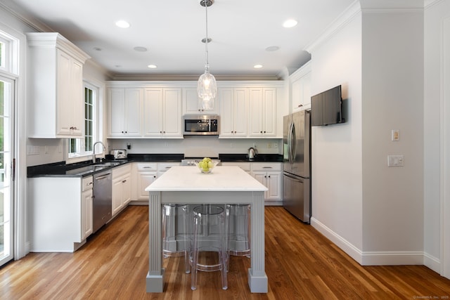 kitchen featuring a kitchen island, decorative light fixtures, white cabinetry, stainless steel appliances, and light hardwood / wood-style flooring