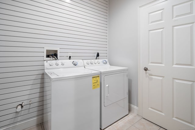 laundry area with light tile patterned floors, washing machine and clothes dryer, and wooden walls