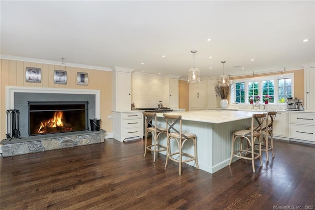 kitchen with a spacious island, pendant lighting, a kitchen bar, a fireplace, and white cabinets