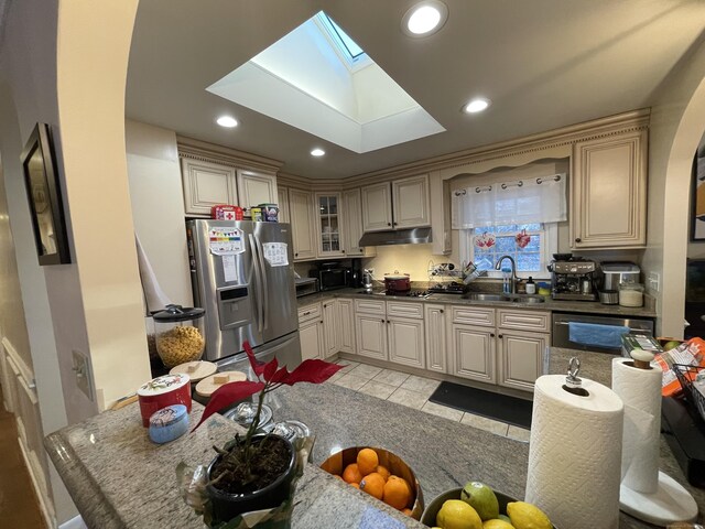 kitchen with sink, light tile patterned floors, stainless steel fridge, a skylight, and cream cabinetry