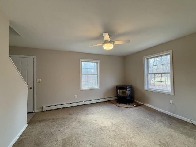 carpeted spare room with ceiling fan, a wood stove, and baseboard heating