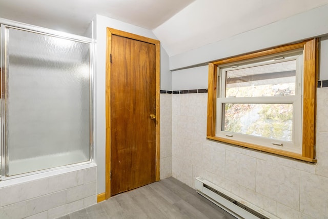 bathroom with wood-type flooring, a baseboard radiator, vaulted ceiling, and enclosed tub / shower combo