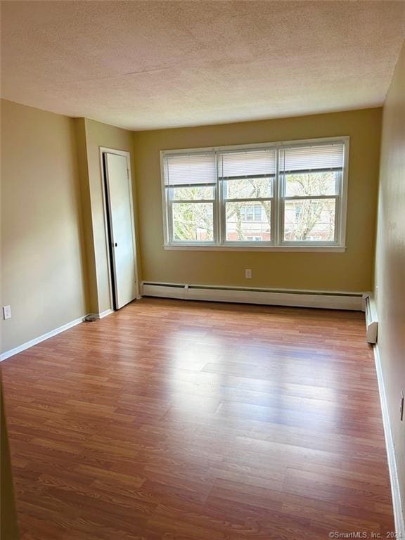 unfurnished room featuring a textured ceiling, a baseboard radiator, and light hardwood / wood-style flooring