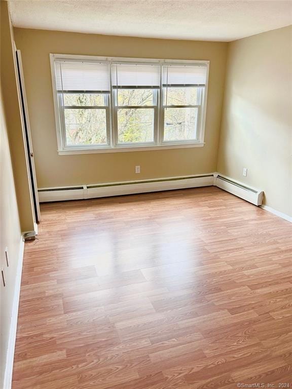 empty room featuring light hardwood / wood-style floors, baseboard heating, and a wealth of natural light