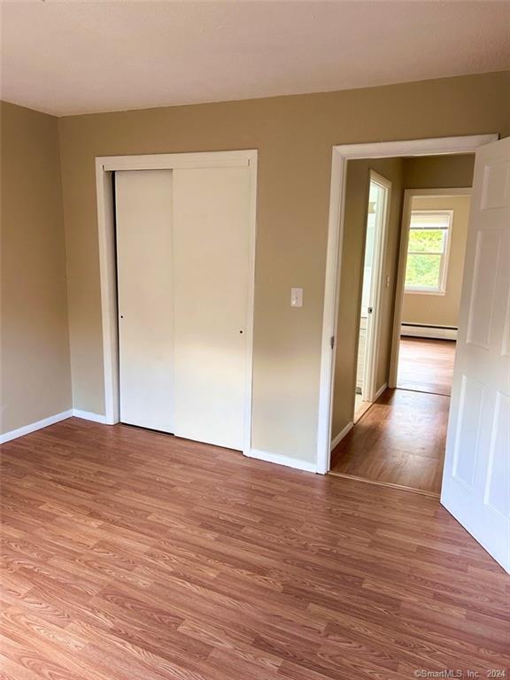 unfurnished bedroom with a baseboard heating unit, a closet, and light hardwood / wood-style flooring