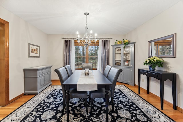 dining space with a textured ceiling, light wood-type flooring, and an inviting chandelier