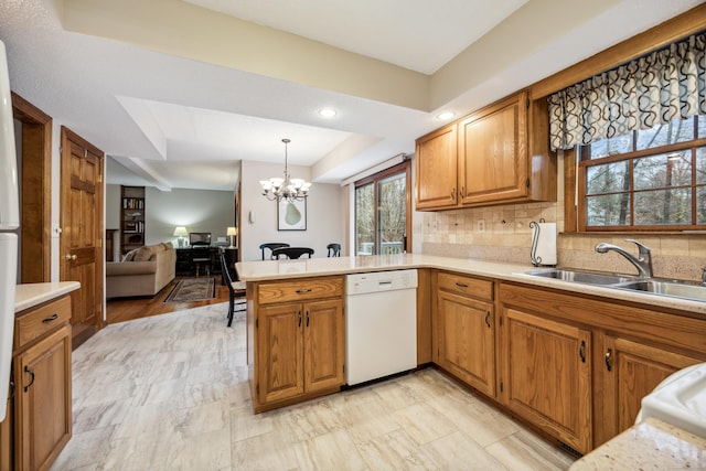 kitchen featuring sink, kitchen peninsula, white dishwasher, a chandelier, and decorative light fixtures