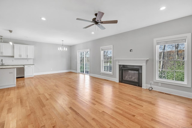 unfurnished living room with a fireplace, ceiling fan with notable chandelier, light hardwood / wood-style floors, and plenty of natural light