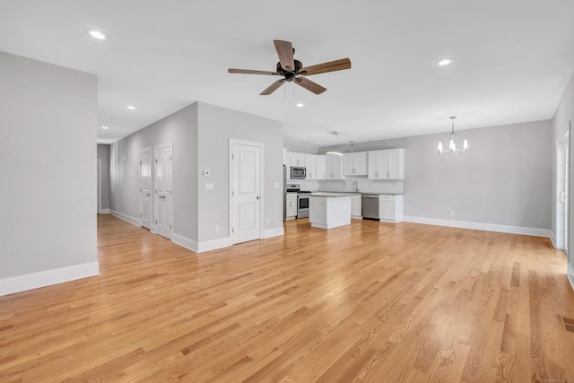 unfurnished living room featuring ceiling fan with notable chandelier, light hardwood / wood-style floors, and sink