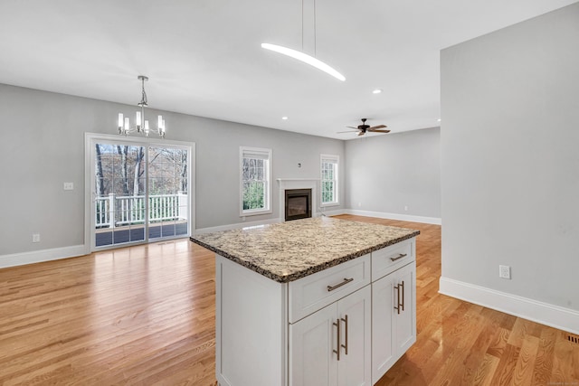 kitchen featuring pendant lighting, a center island, white cabinets, ceiling fan with notable chandelier, and light stone countertops