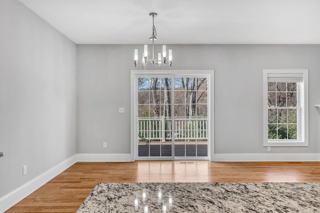 unfurnished dining area with hardwood / wood-style flooring, an inviting chandelier, and a wealth of natural light