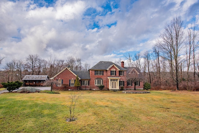 view of front of house with a chimney, brick siding, and a front yard