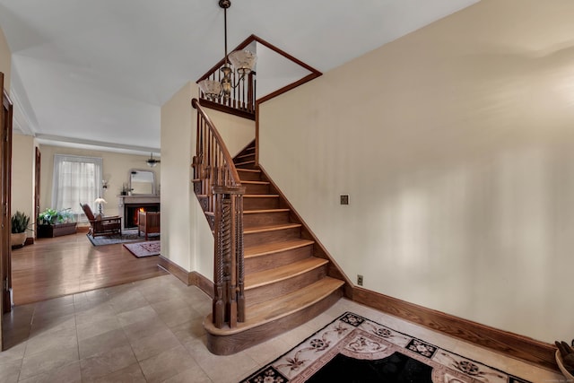 staircase with baseboards, a lit fireplace, and tile patterned floors
