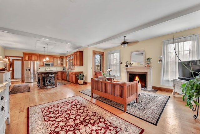 living room with a warm lit fireplace, light wood finished floors, baseboards, and ceiling fan