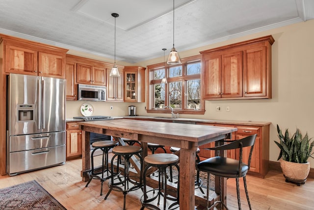 kitchen featuring appliances with stainless steel finishes, ornamental molding, sink, decorative light fixtures, and light hardwood / wood-style flooring