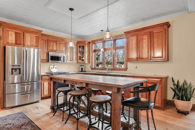 kitchen featuring light wood finished floors, stainless steel appliances, a sink, brown cabinetry, and decorative light fixtures