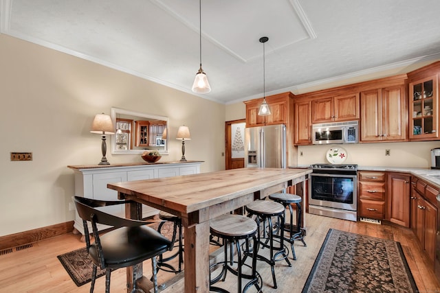 kitchen with pendant lighting, crown molding, appliances with stainless steel finishes, light hardwood / wood-style floors, and a kitchen bar