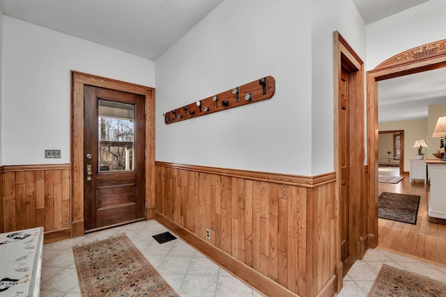 doorway with wainscoting, wood walls, and light tile patterned flooring