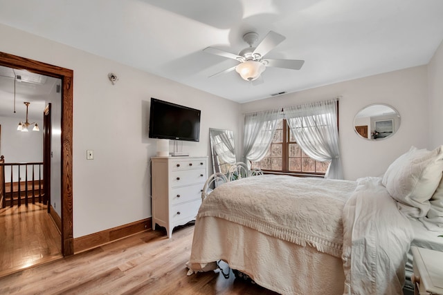 bedroom featuring ceiling fan with notable chandelier and light wood-type flooring