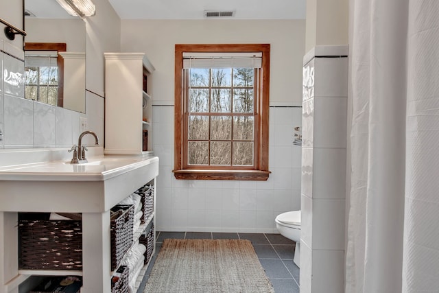 full bathroom with a wealth of natural light, toilet, tile patterned flooring, and tile walls